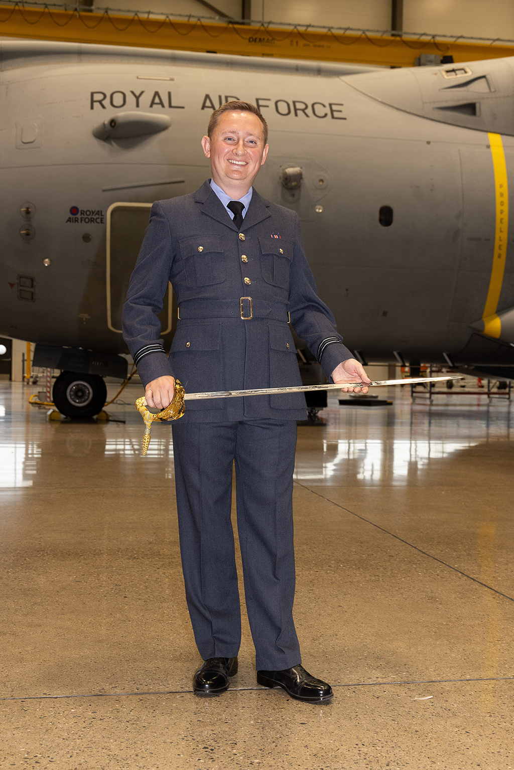 Flight Lieutenant Ewers stands at ease, while proudly holding the Logistics Profession’s Gill Sword horizontally, in both hands